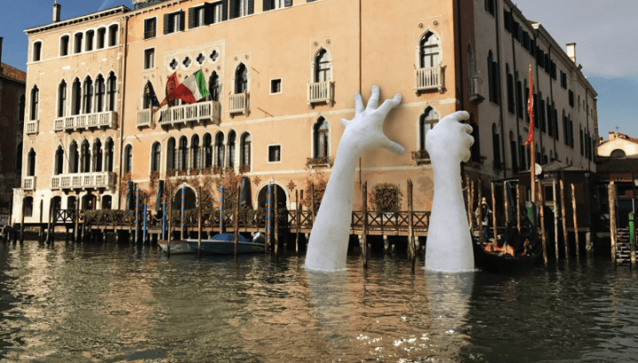 A statue of hands reach out to a building in Venice, Italy.  An example of an artist's imagination 
